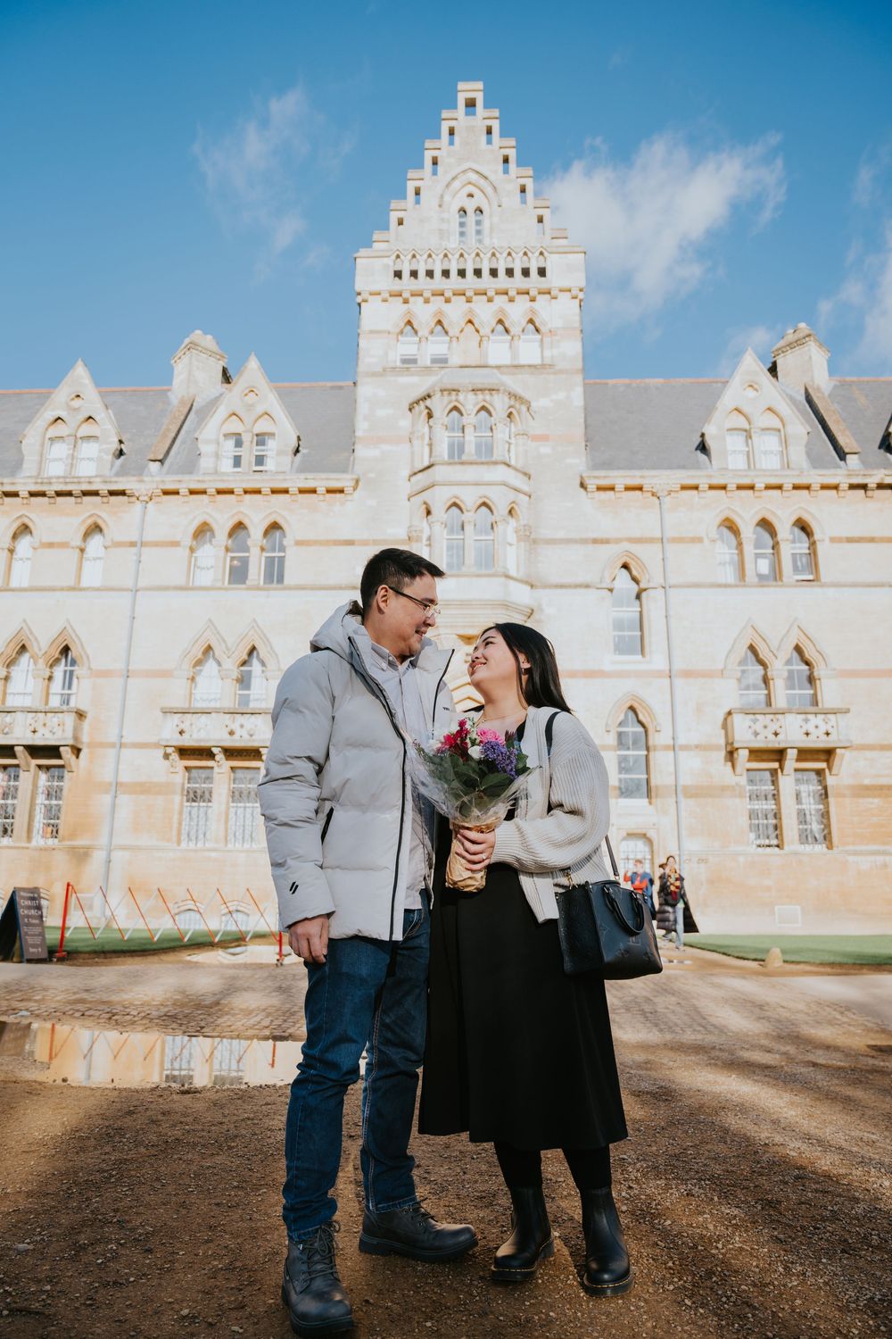 A couple shares sweet romantic moments outdoors in front of an ornate white Gothic Revival church building on a sunny day.
