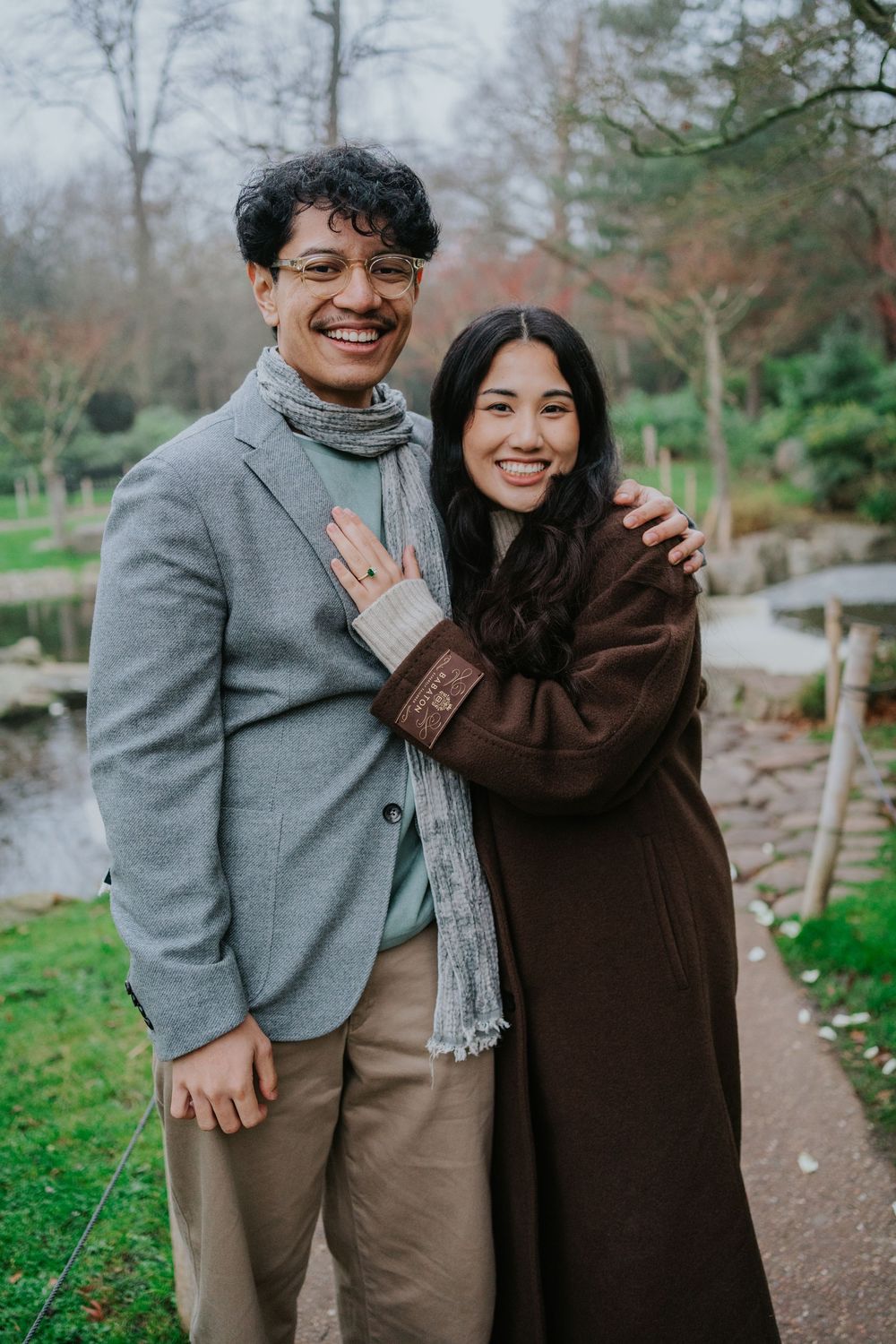 Two people sharing a warm embrace while laughing together on a garden path during autumn.