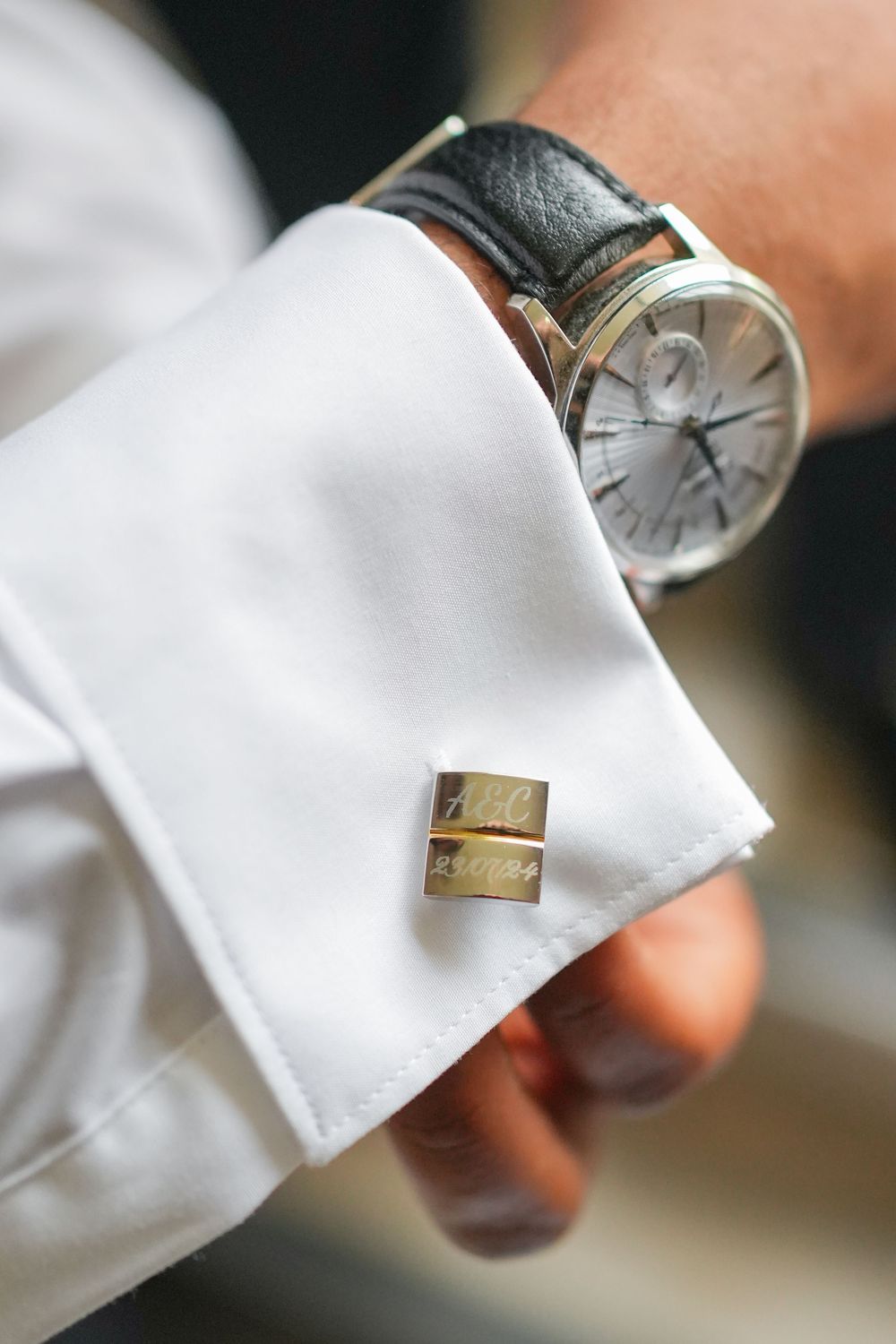 Close-up view of an elegant wristwatch with leather strap and silver cufflink on crisp white dress shirt sleeve.