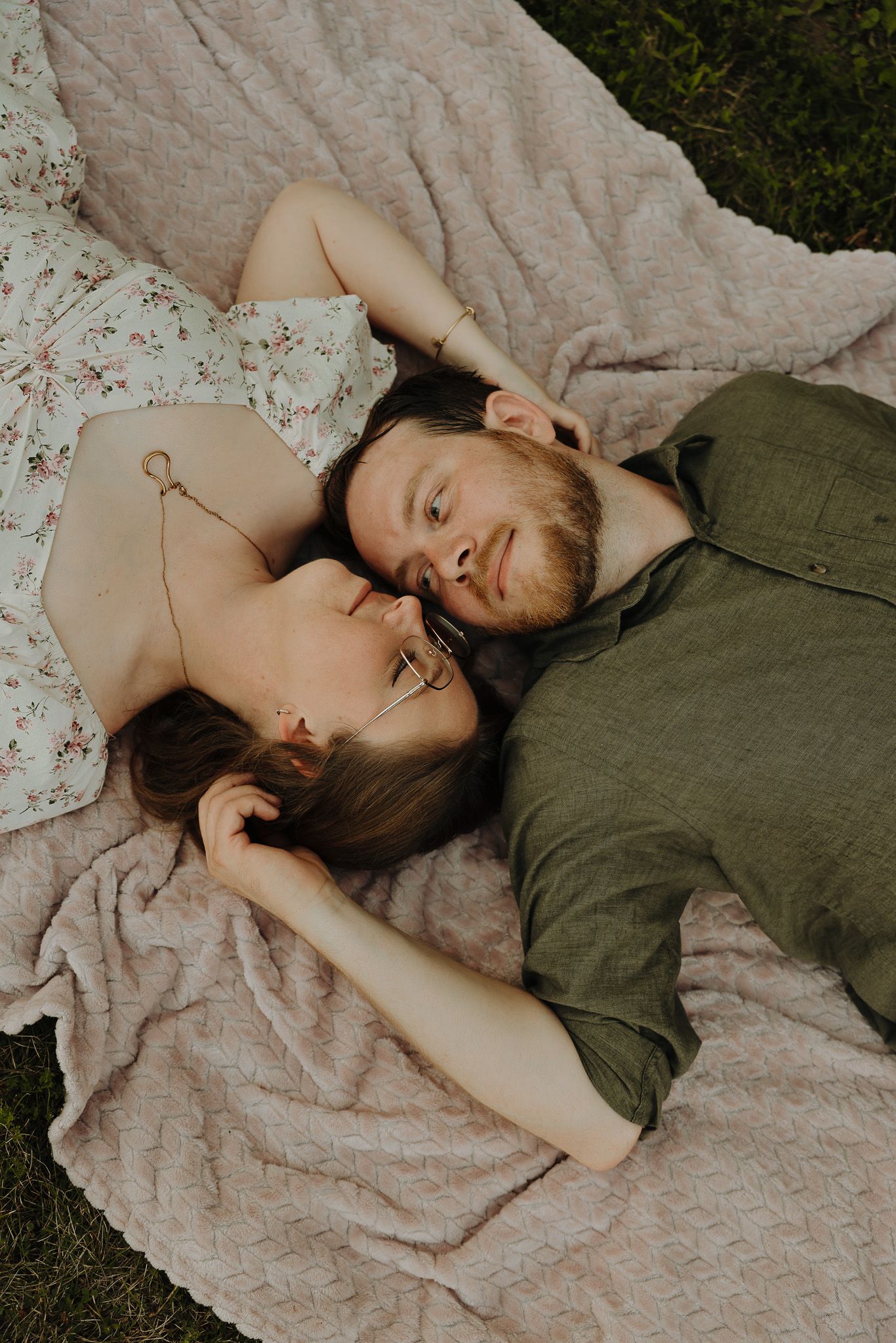 Couple lying on a floral blanket in casual attire during an outdoor photo session.