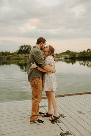 A romantic moment shared between a couple on a wooden dock by a serene lake during sunset.