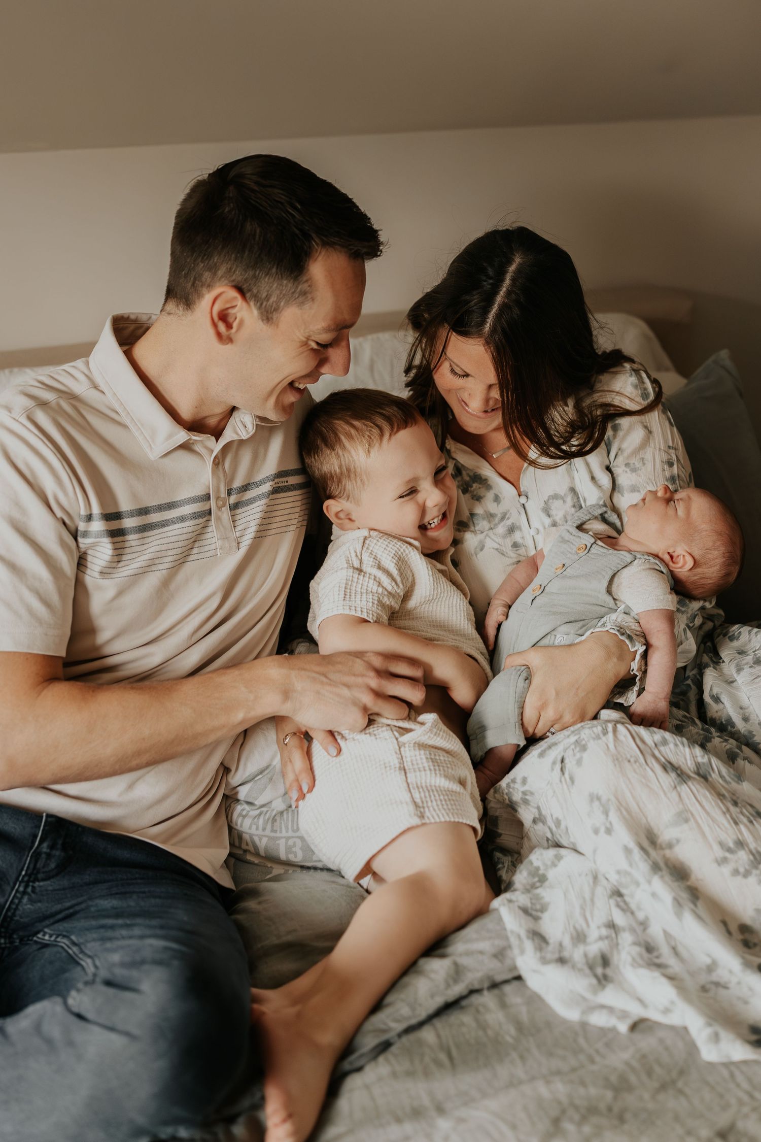 A family shares an intimate moment together while relaxing on a bed with neutral tones and soft lighting.