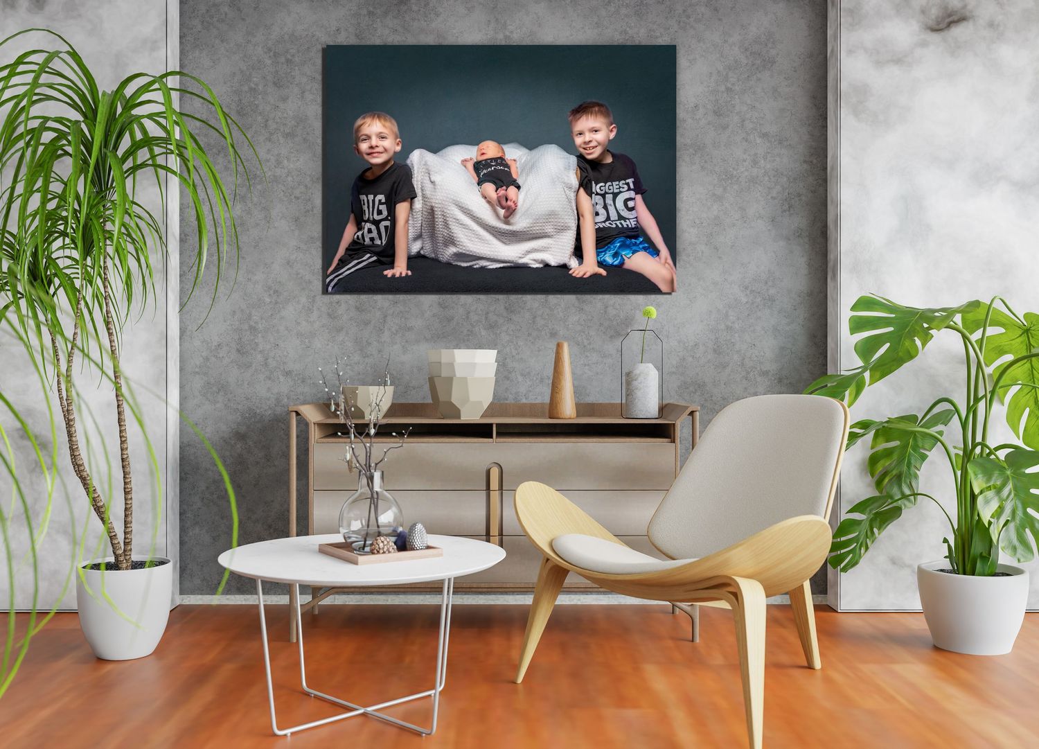 Three siblings wearing matching Big Cat shirts pose together with a newborn baby swaddled in white on blue sofa.