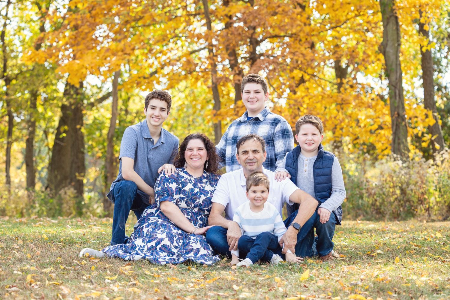 Three children share a joyful embrace while standing on an autumn path surrounded by golden fall foliage.