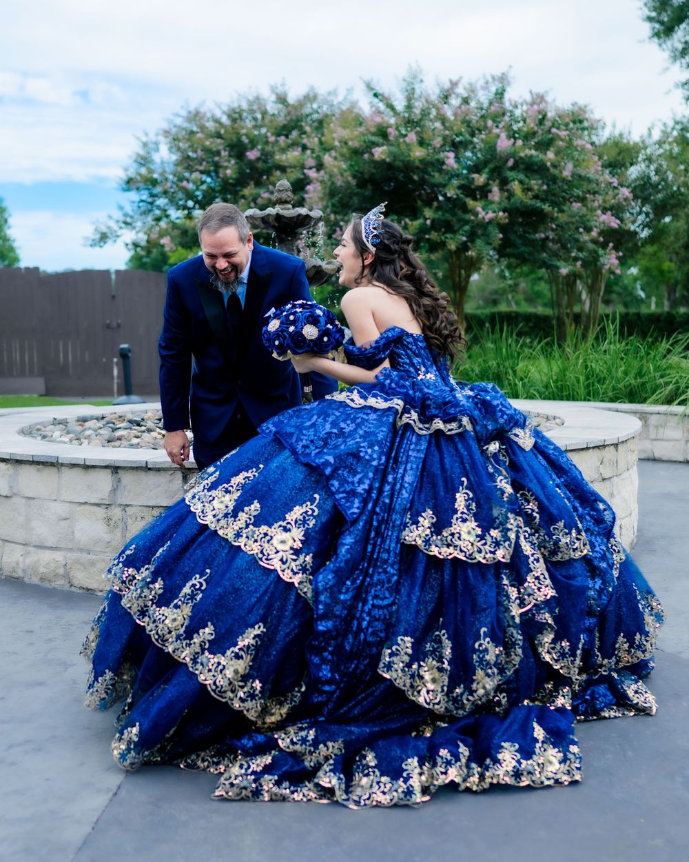A couple in formal attire share a moment, with the woman wearing an elaborate royal blue and silver quinceañera ball gown.