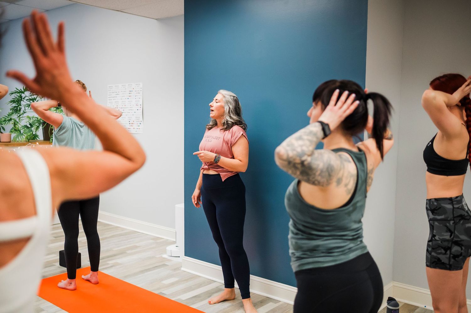 A yoga or fitness class practicing stretching exercises together on orange mats in a studio space.
