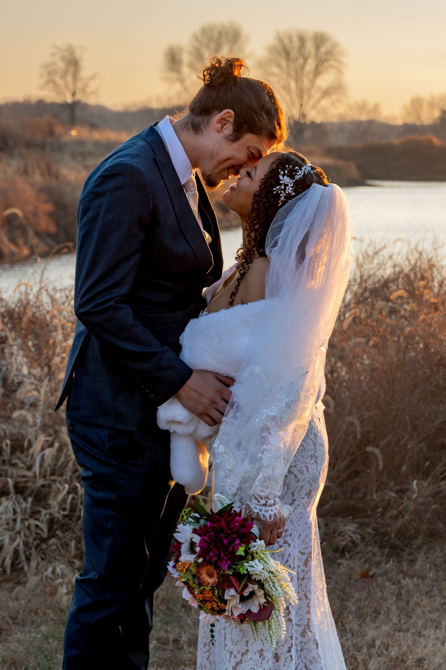 Newlyweds embracing in golden sunset light with autumn field backdrop.