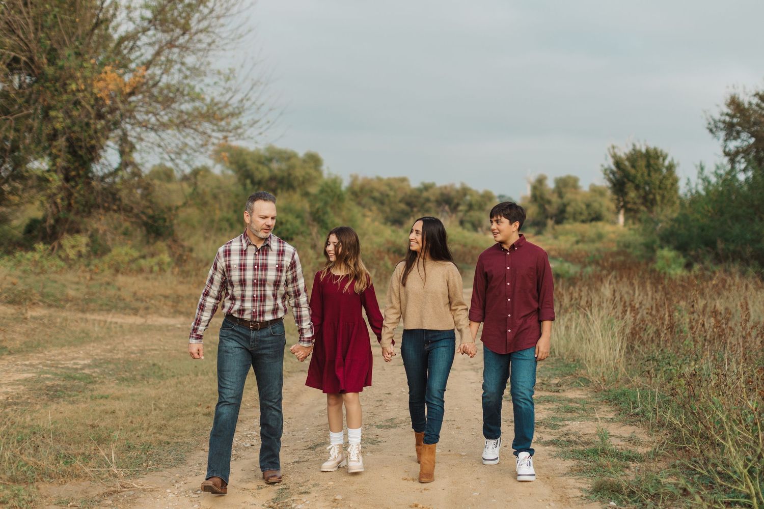 A family walking together on a rustic autumn path surrounded by fall foliage and white fencing.