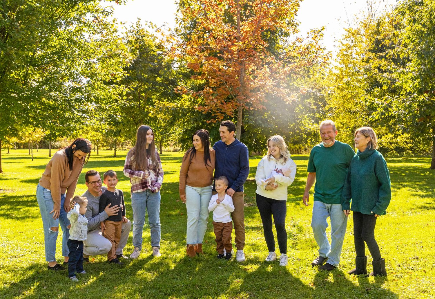 A large family shot with multiple family groupings with fall leaves in the background all looking at one another