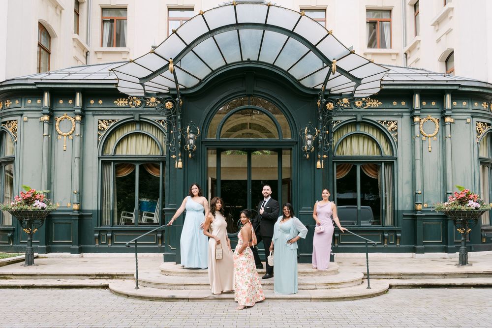 A group stands on steps in front of an elegant Art Nouveau entrance with ornate green metalwork and glass canopy.