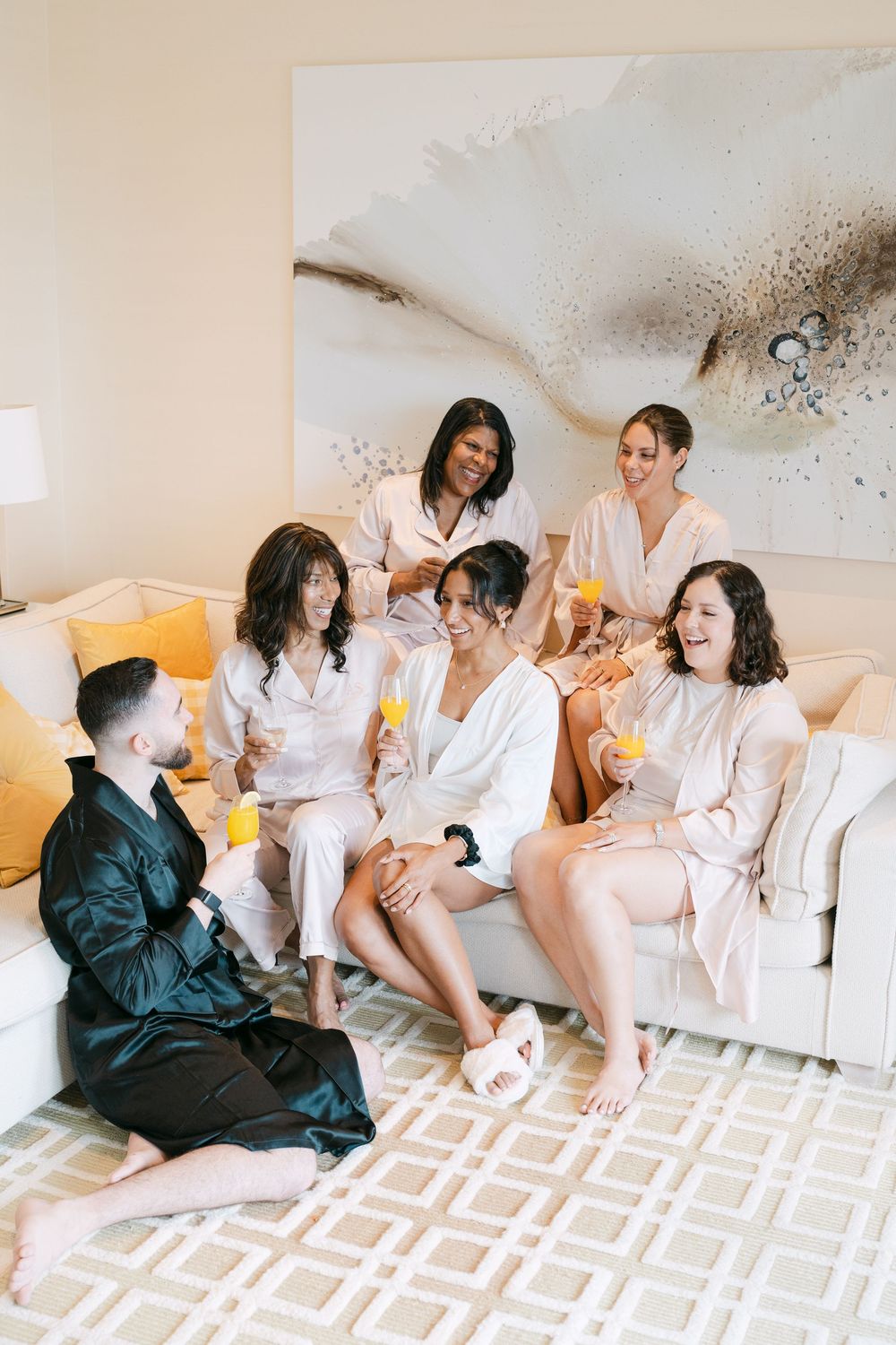 A group gathering in robes and loungewear sits together on a white couch for pre-wedding preparations.