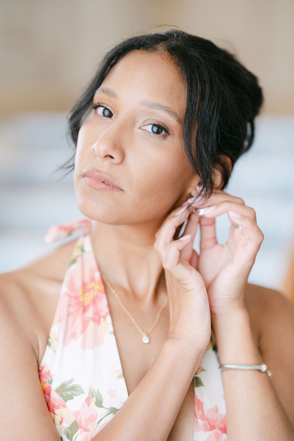 A close-up portrait showing elegant jewelry and a floral dress against a soft background.