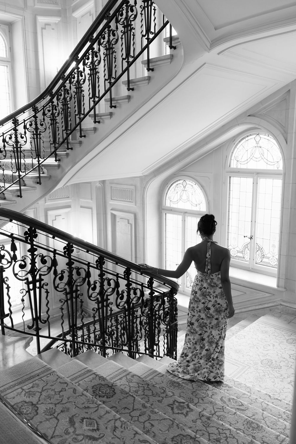 Elegant black and white photo of a grand staircase with ornate railings and arched windows in a historic building.