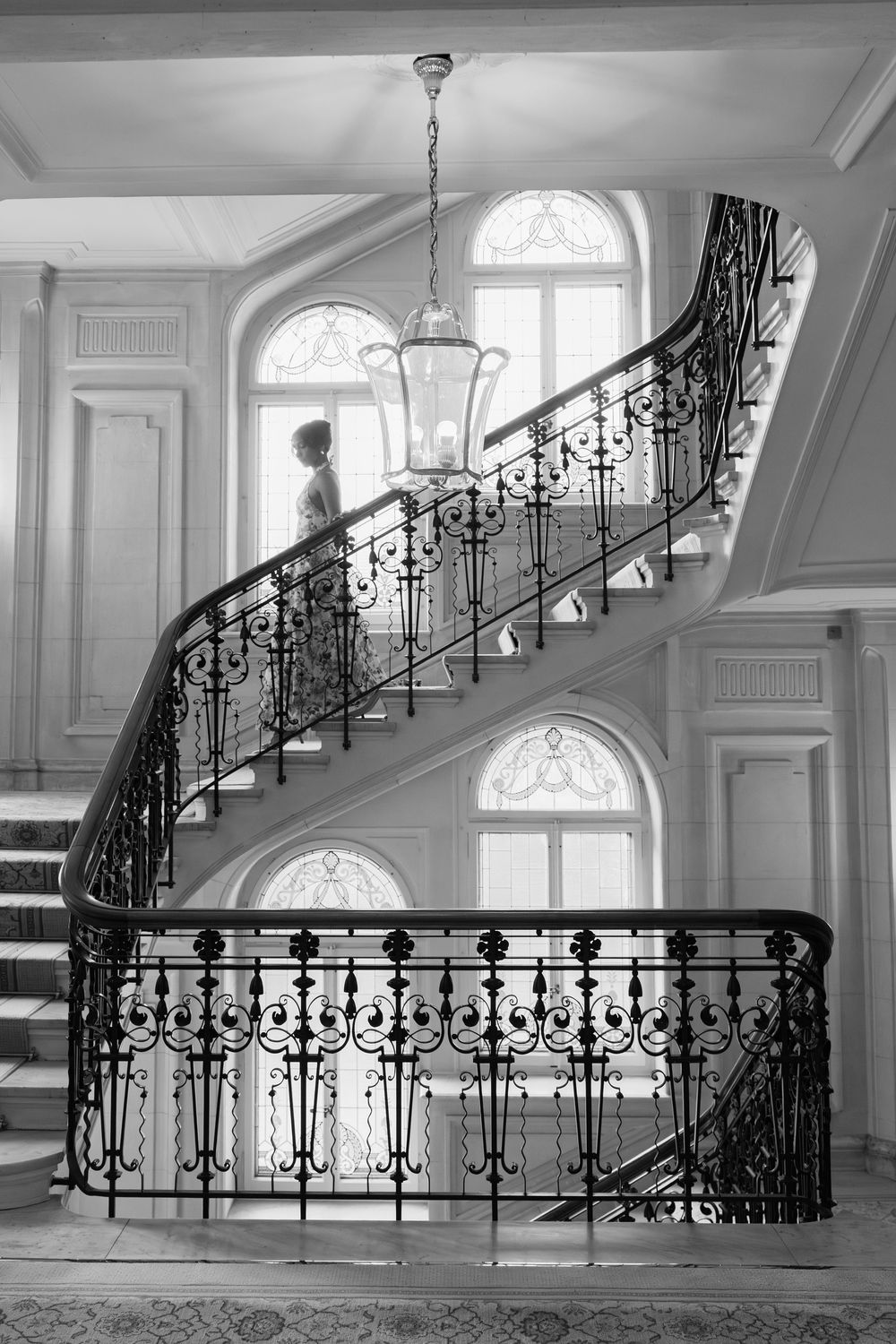 Elegant white curved staircase with ornate black wrought iron railings and arched windows in a classic interior.