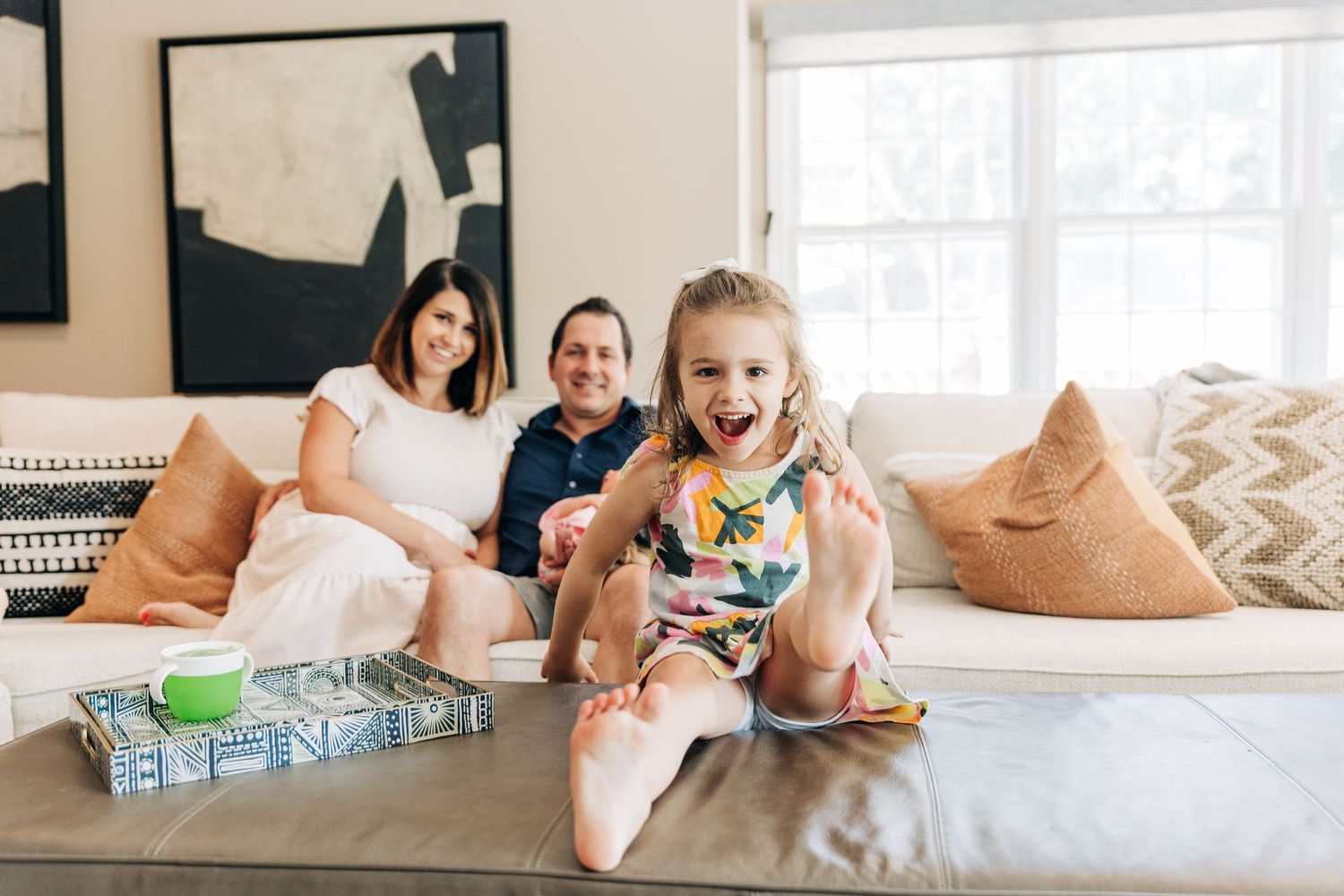 Family relaxing together on a gray couch with throw pillows in a bright living room.