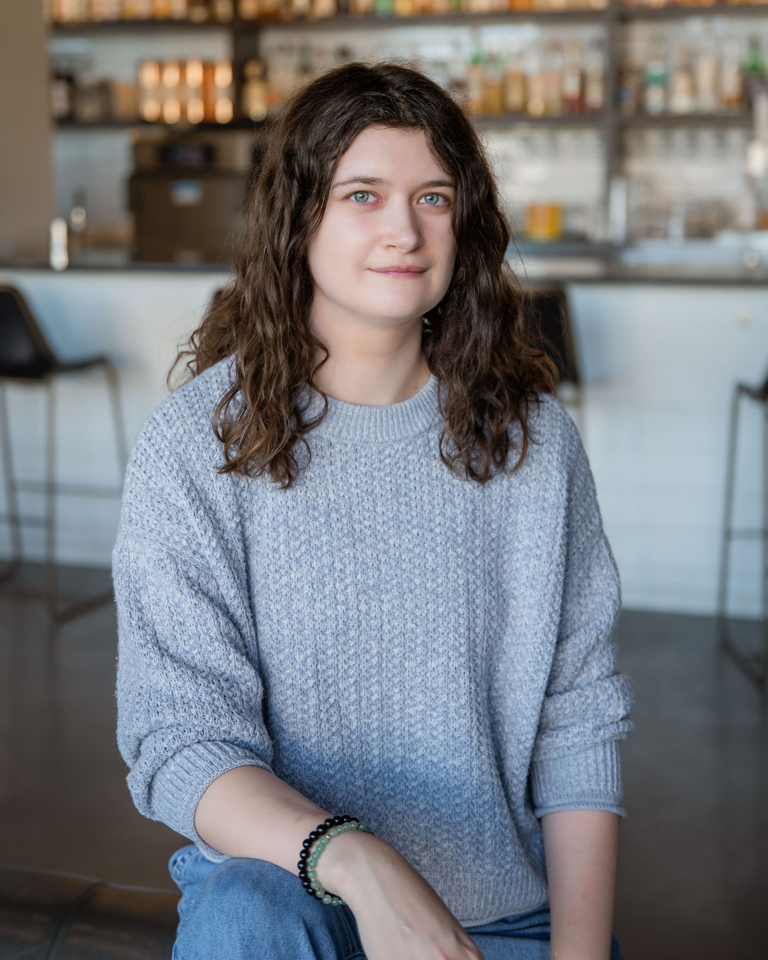 Someone wearing a cozy grey knit sweater sits in a restaurant with a bar counter and bottles visible in background.