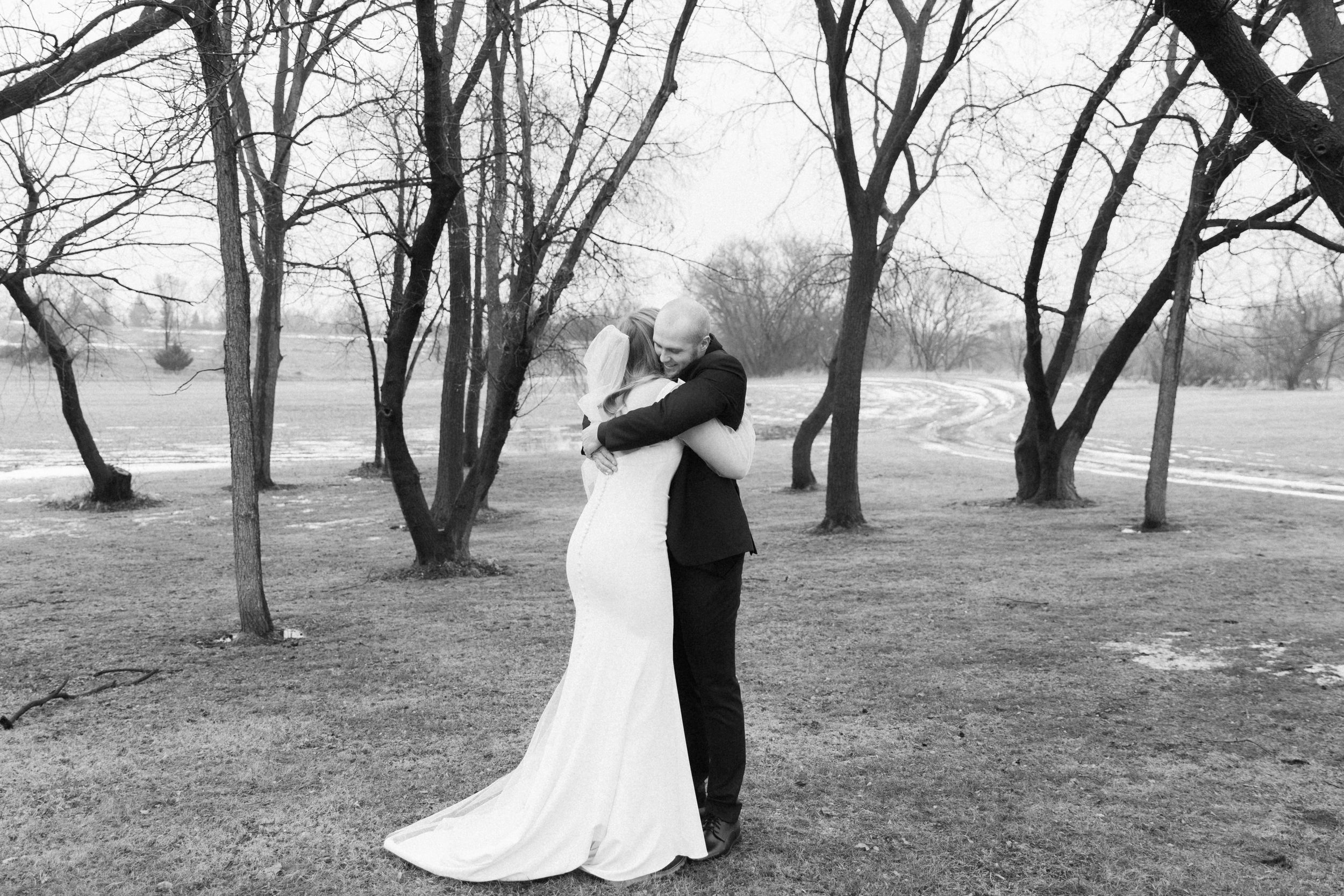 Black and white photo of wedding couple sharing intimate moment in winter park landscape.