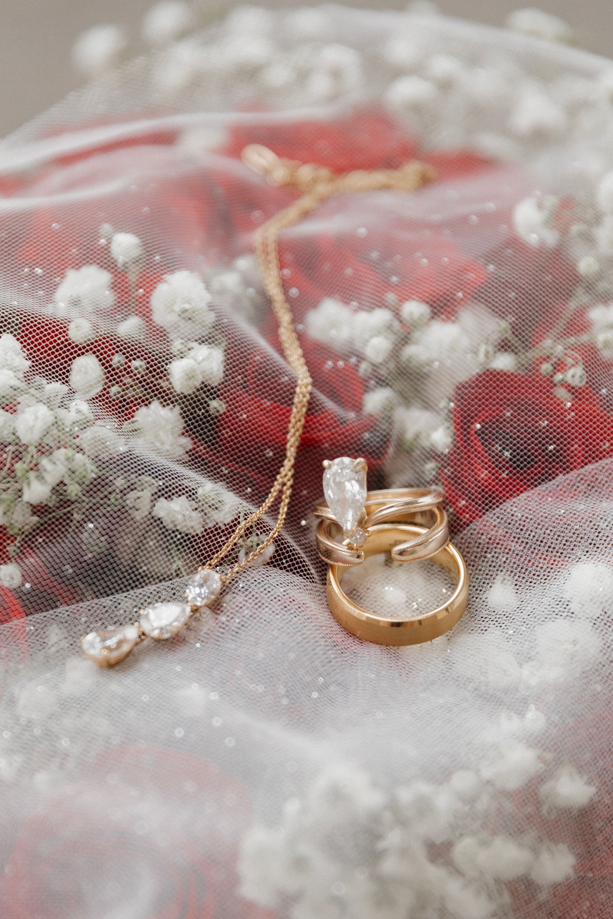 Wedding rings and delicate jewelry rest on white lace with baby's breath flowers creating a romantic bridal detail.
