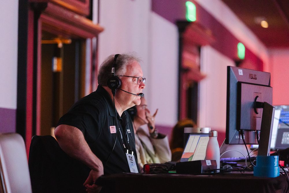 Audio engineer working at a mixing console with headphones in a dimly lit production environment.