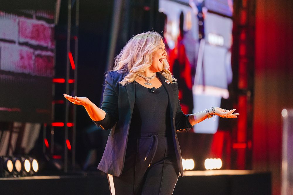 Dynamic performer in black outfit gestures expressively on stage with dramatic red lighting in background.