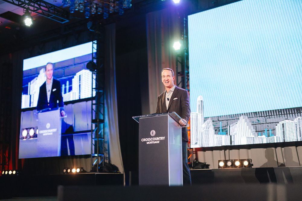 Blue-lit conference stage setup with multiple large display screens showing presentations at a corporate event.