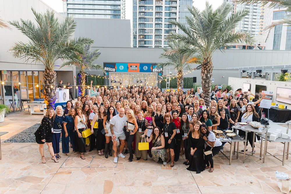 Large group of conference or event attendees gathered together for photos in an outdoor setting with palm trees.