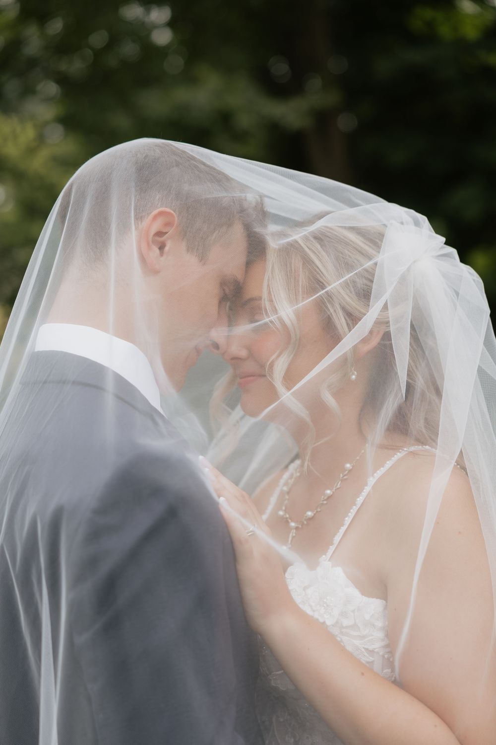 Bride and groom sharing an intimate moment under a flowing white wedding veil outdoors.