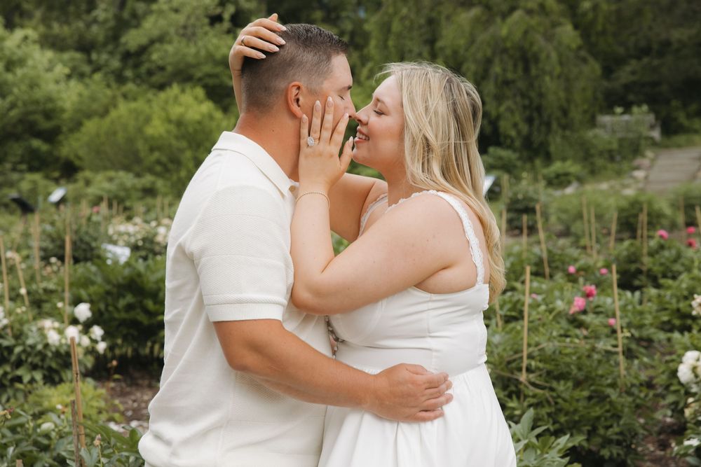 Couple in white outfits sharing a romantic moment in a lush garden, woman touching man's face tenderly.
