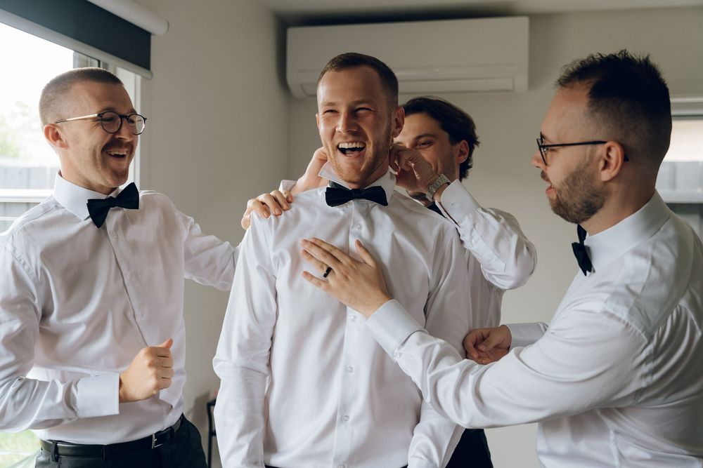 Groomsmen laughing and celebrating while getting ready in white shirts and bowties.