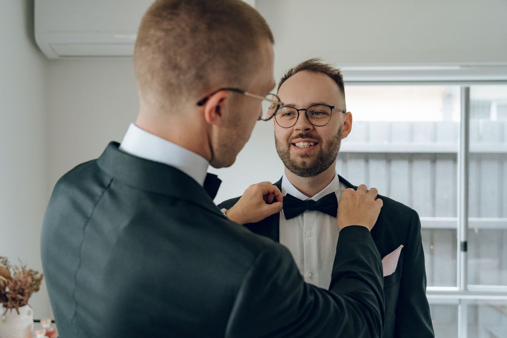 Two people adjusting formal bowties during wedding preparations.