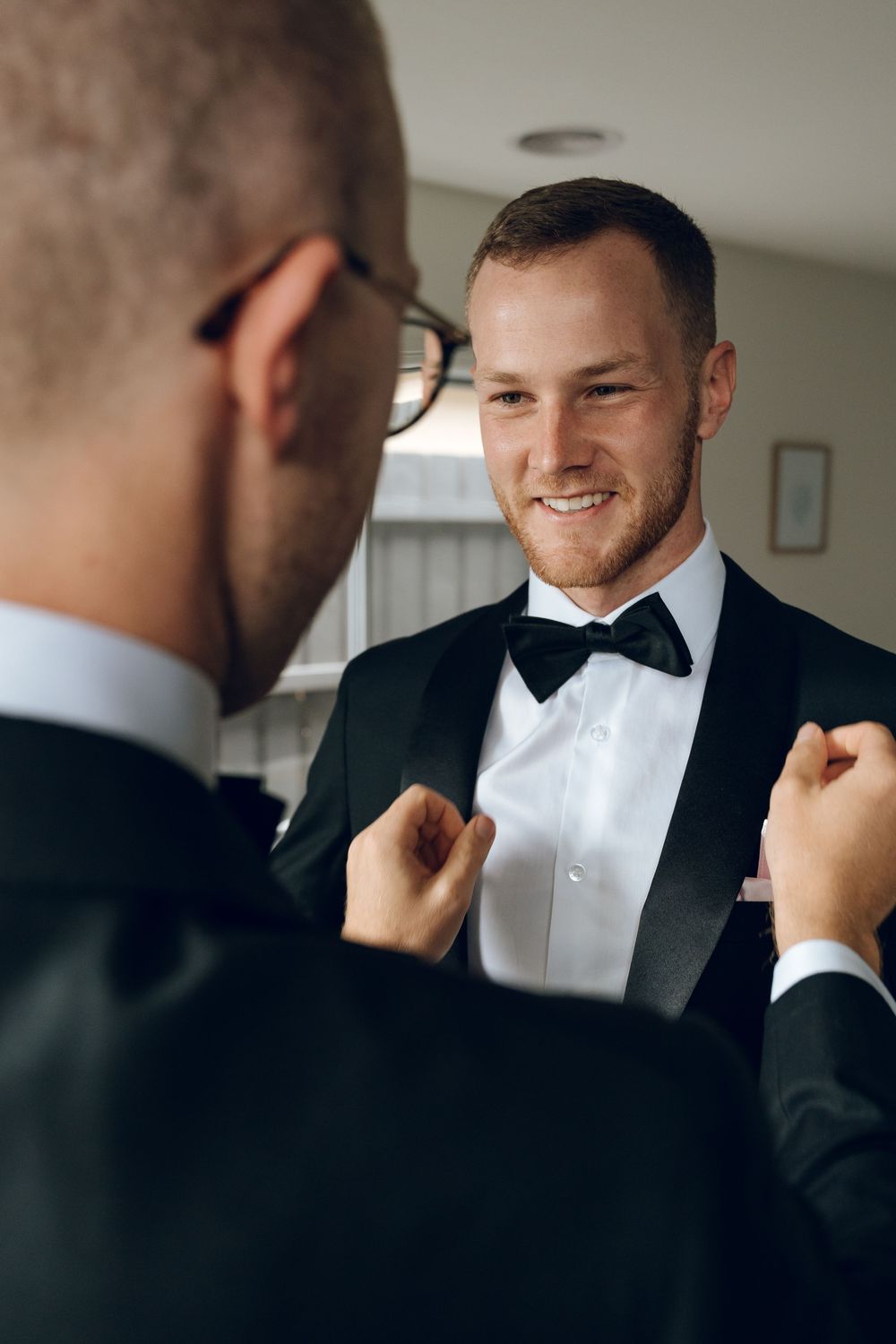 Wedding preparations showing two men in tuxedos adjusting formal attire.