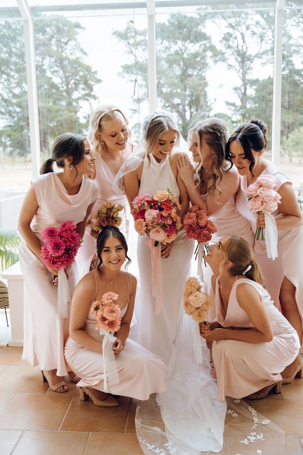 Bridal party in pink dresses gather around bride holding vibrant bouquets.