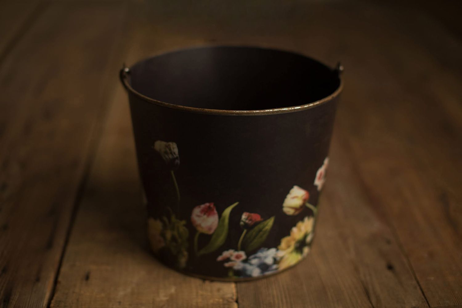 Black decorative planter with floral motif design sits on wooden surface in warm lighting.