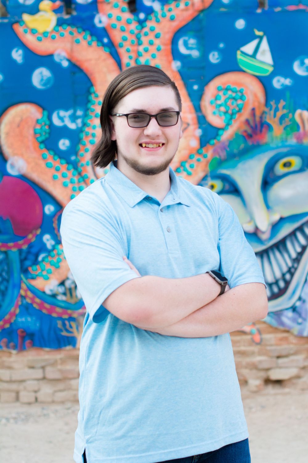 Someone stands with crossed arms in front of a vibrant street art mural featuring sea creatures and nautical elements.
