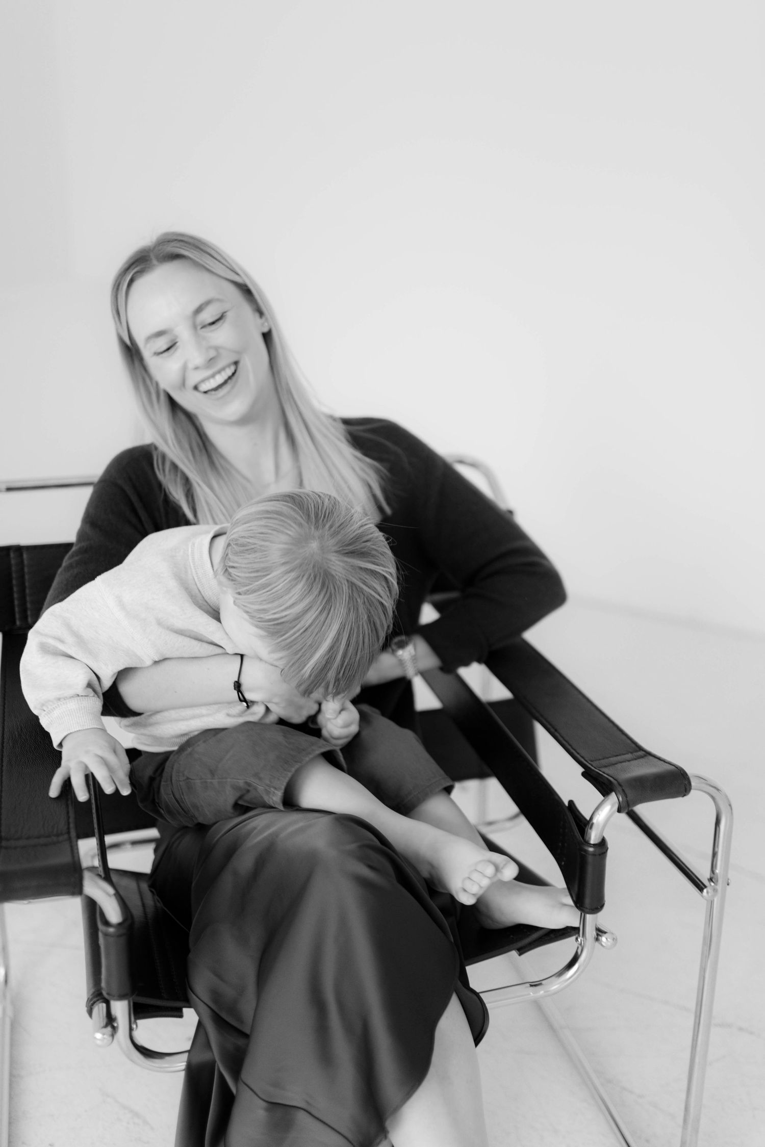 A joyful candid moment of parent and small child laughing together while sitting in a bright white room.