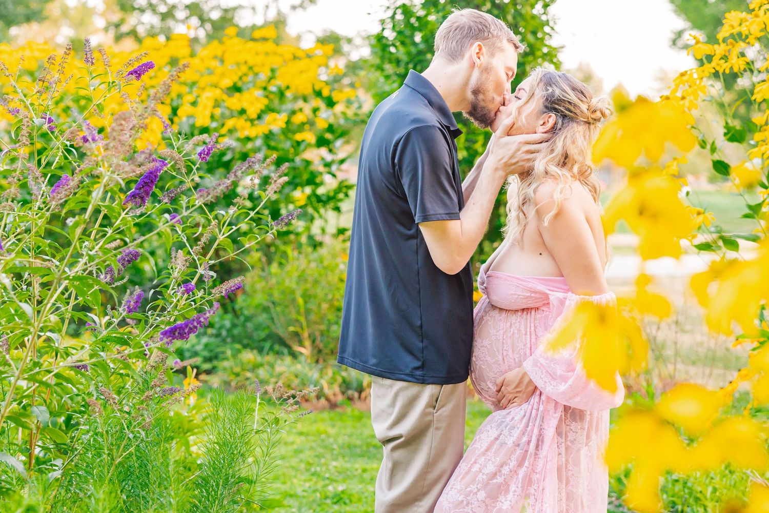 A romantic couple shares a tender moment in a vibrant garden filled with yellow and purple wildflowers.