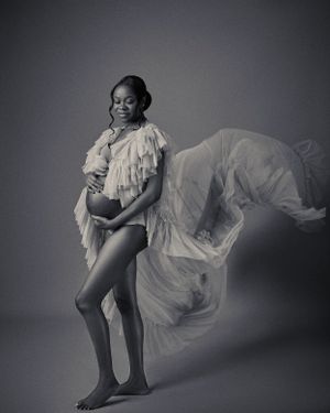 a black and white photograph of pregnant lady with flowwing dress.