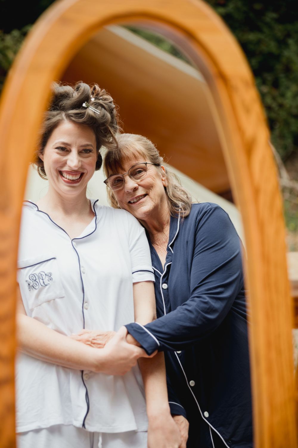 Two people share a joyful moment framed by a wooden mirror in an outdoor setting.