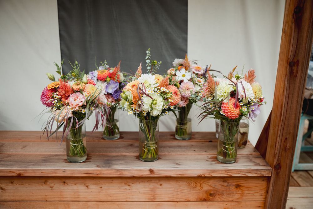 Colorful wedding flower arrangements in mason jars displayed on wooden table.