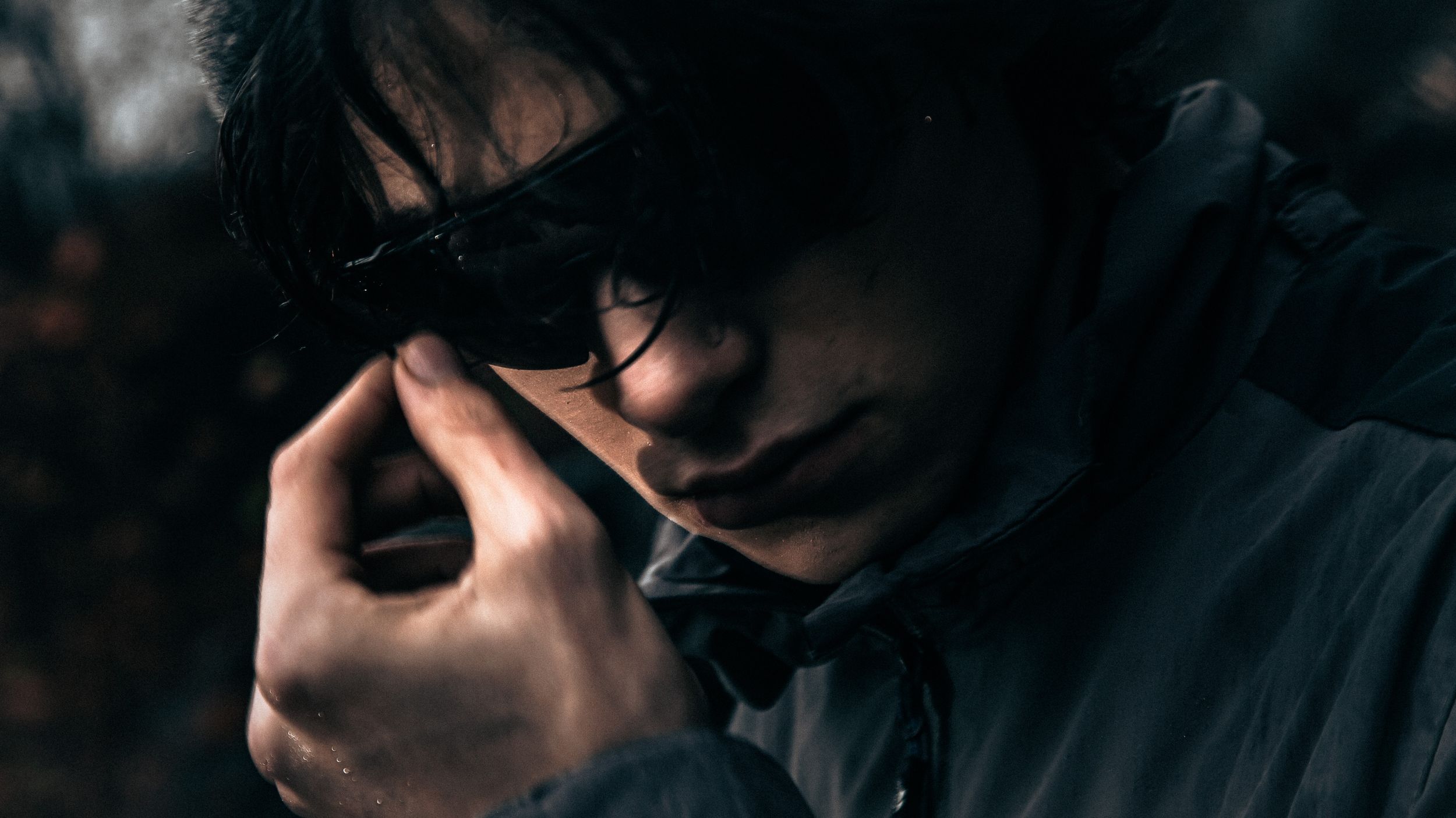Moody close-up portrait with sunglasses in dark atmospheric lighting.
