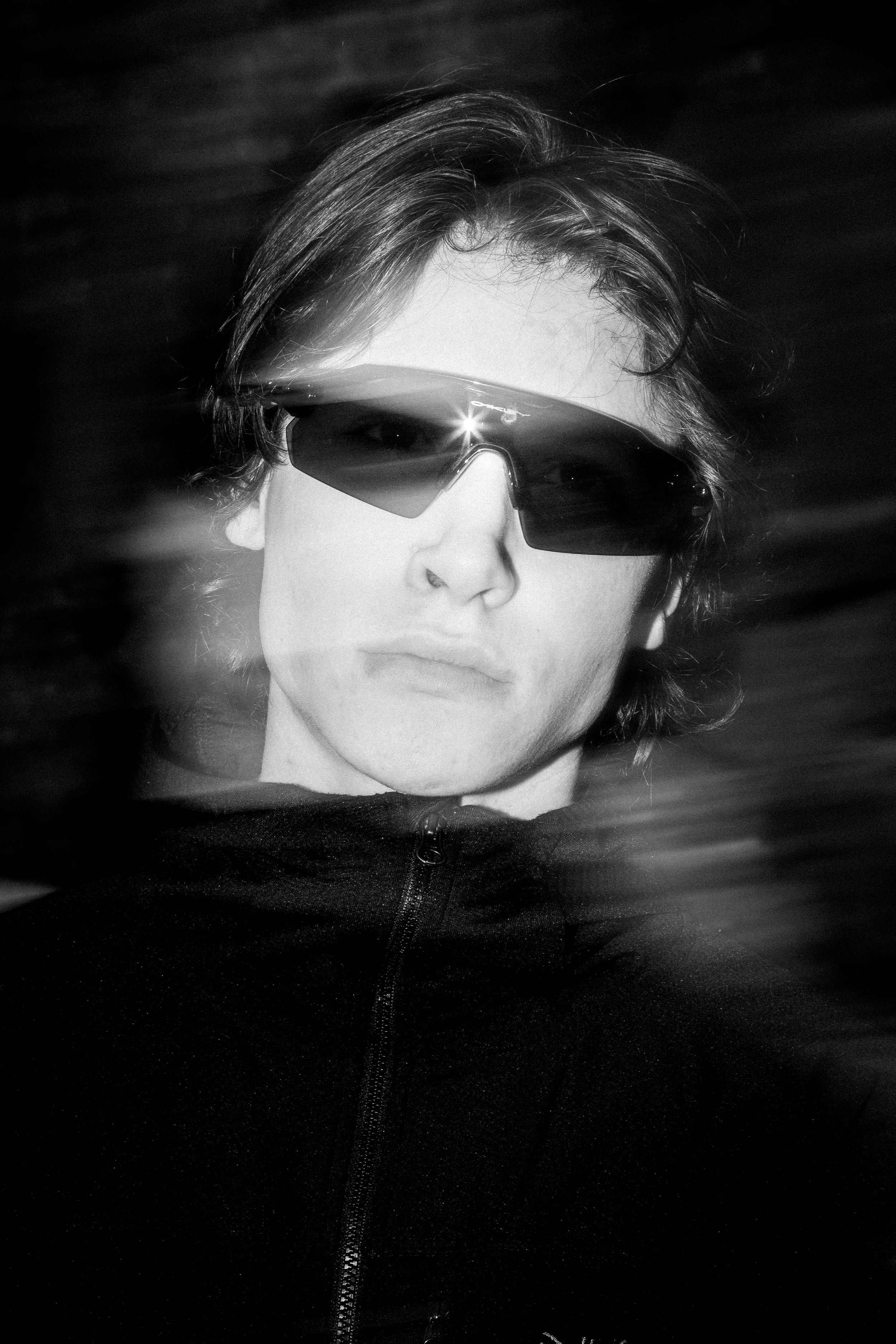 A dark and moody black and white portrait with dramatic side lighting and sunglasses.
