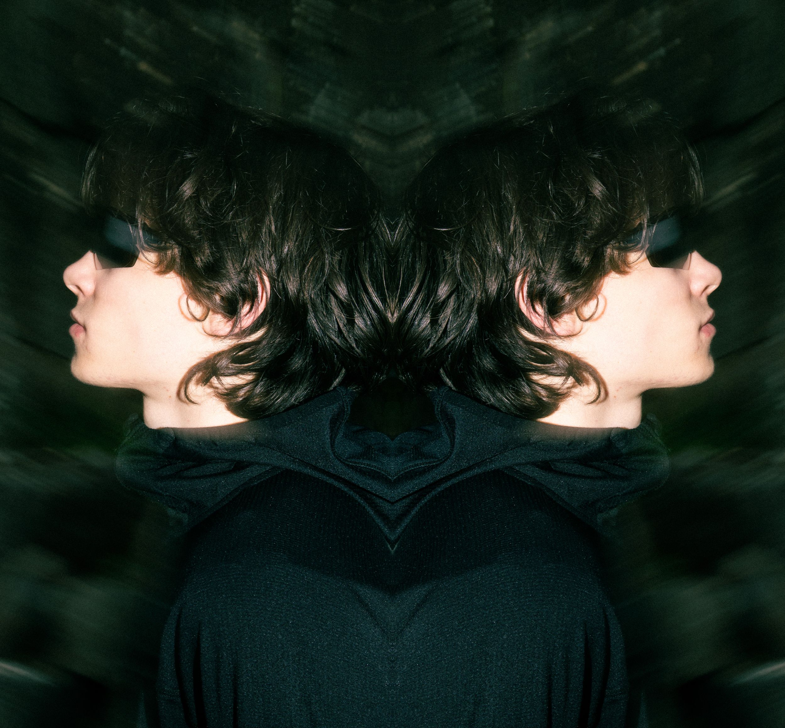 Artistic mirrored profile portrait against dark ethereal background.
