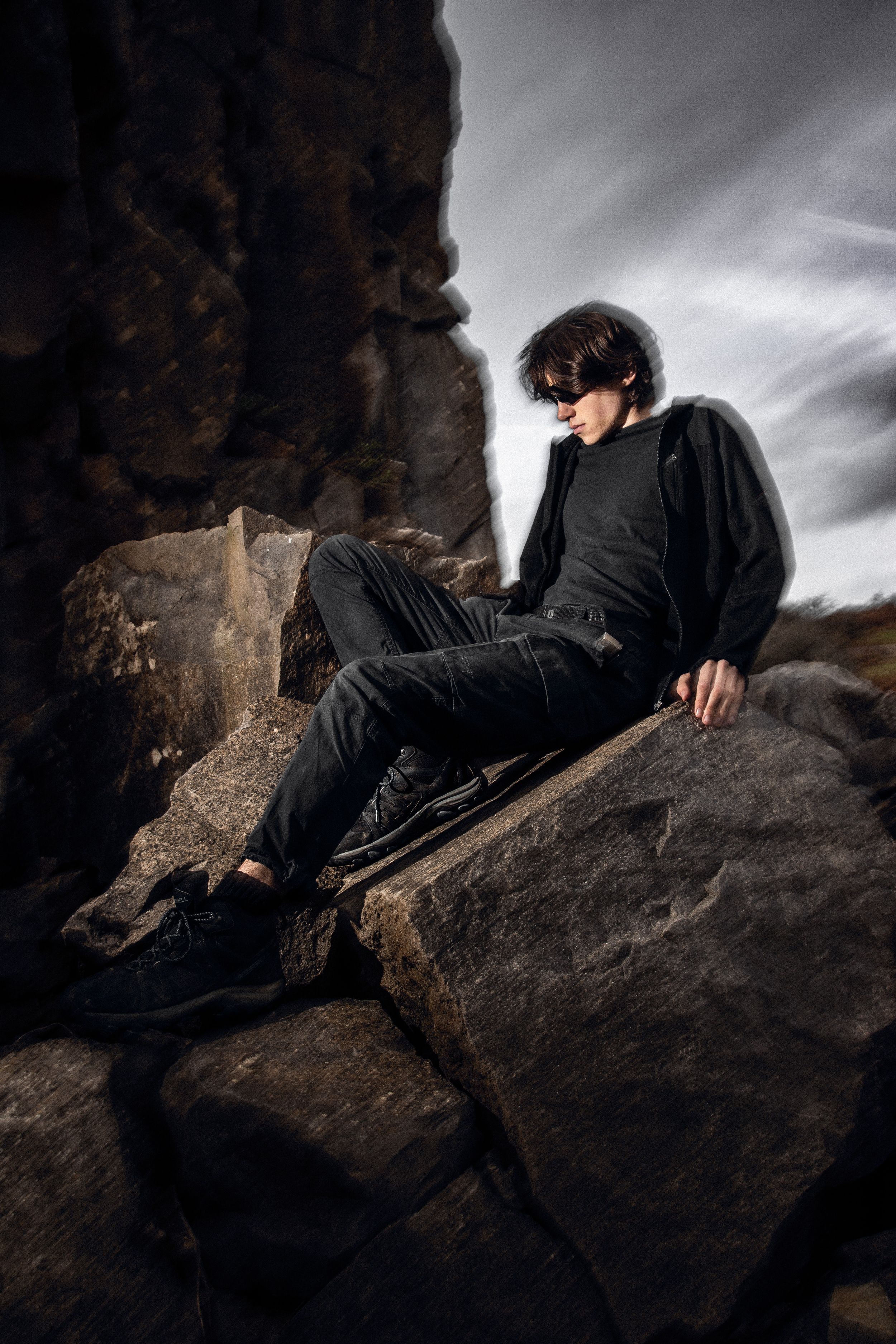 Dramatic fashion portrait on rocky terrain against stormy sky.