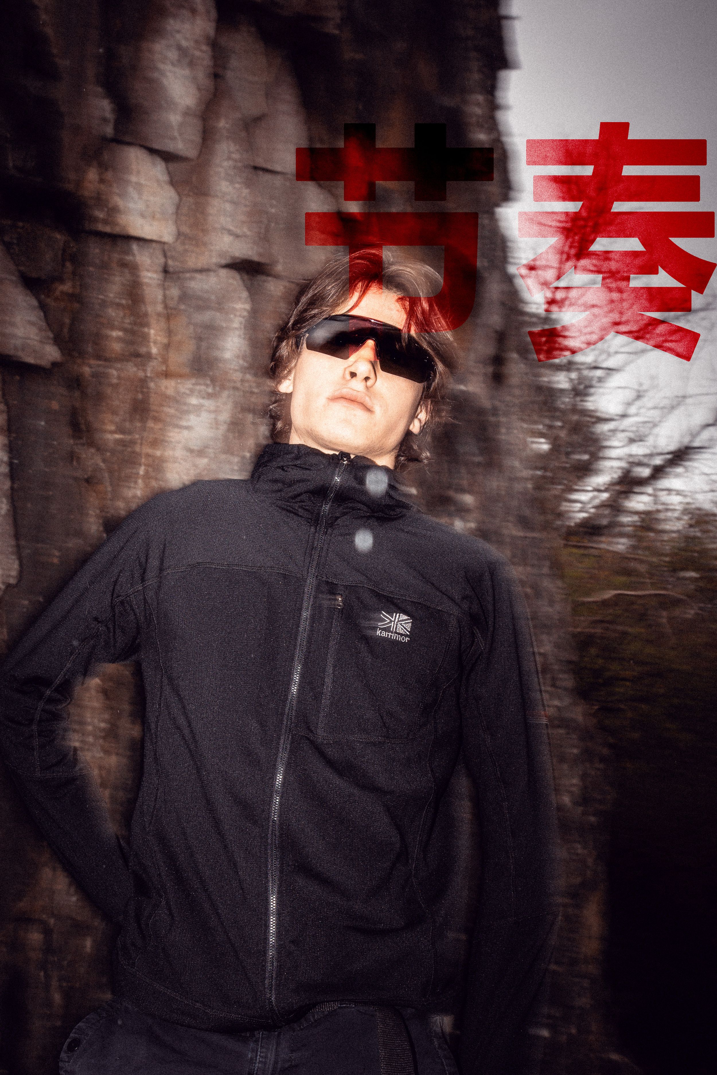 Figure in black jacket against rock wall with red graphic overlay effects.