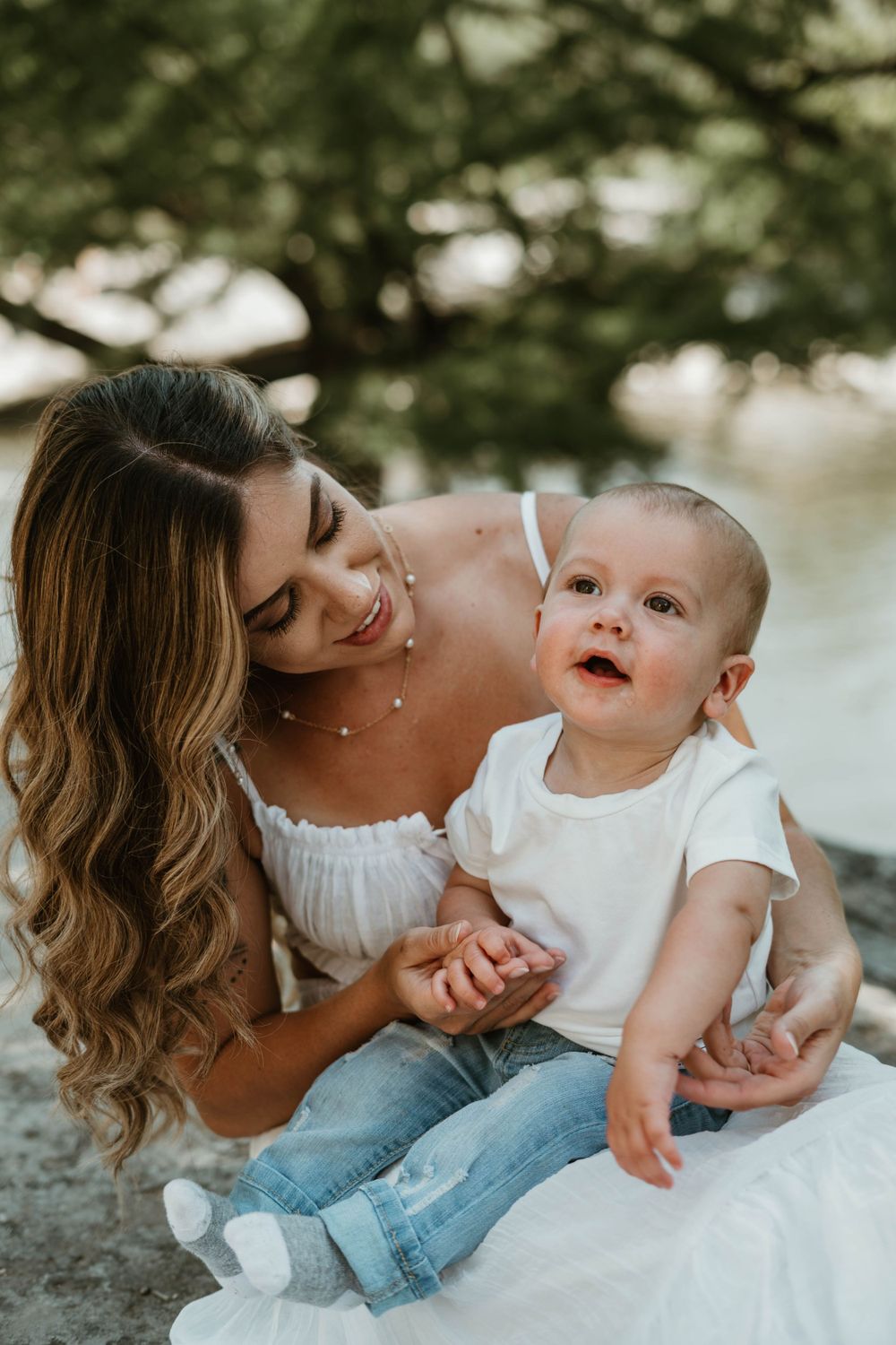 A tender moment between parent and baby on a rocky surface by the water.