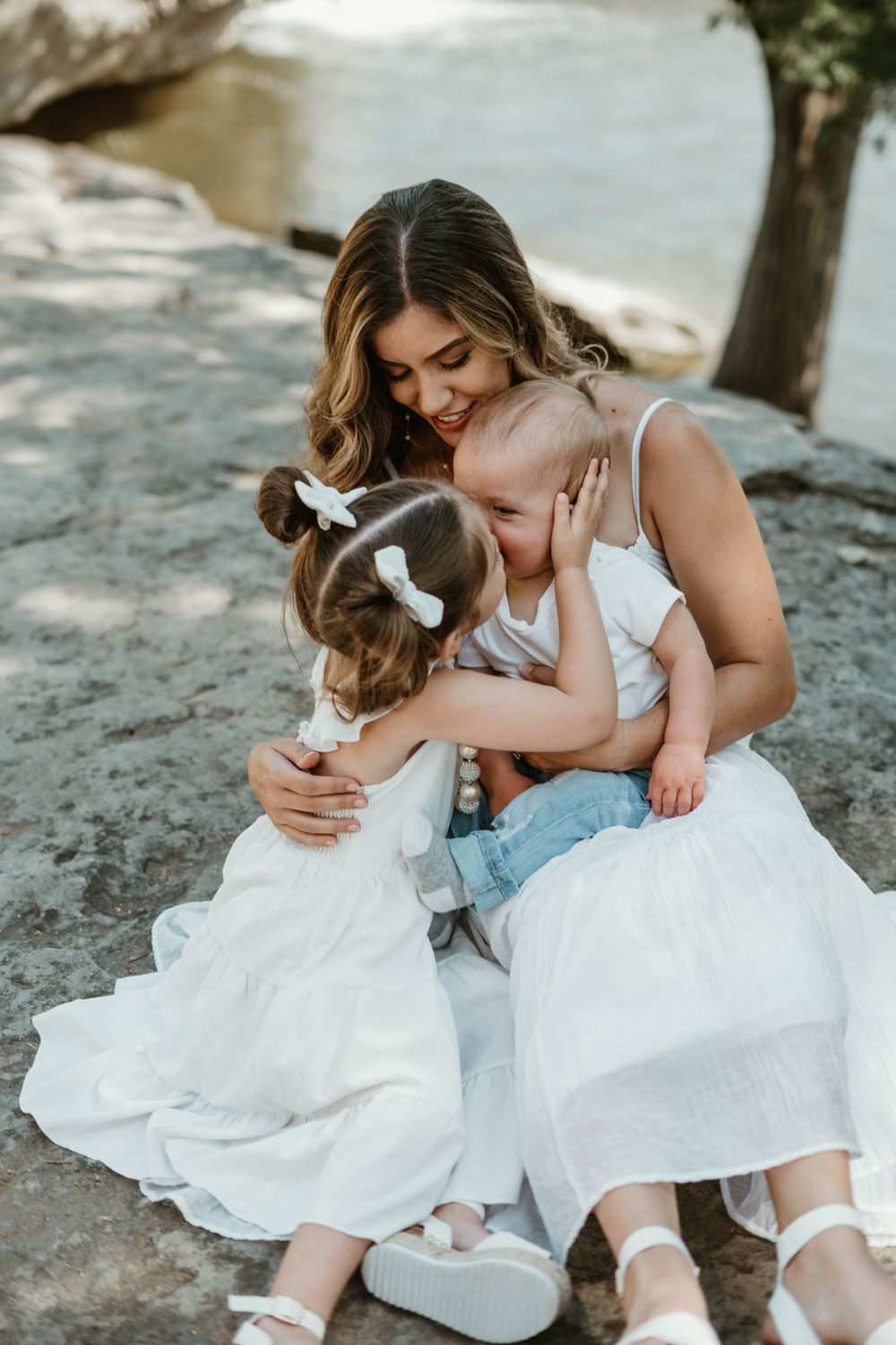 A tender family moment captured outdoors as they embrace on a rocky surface.