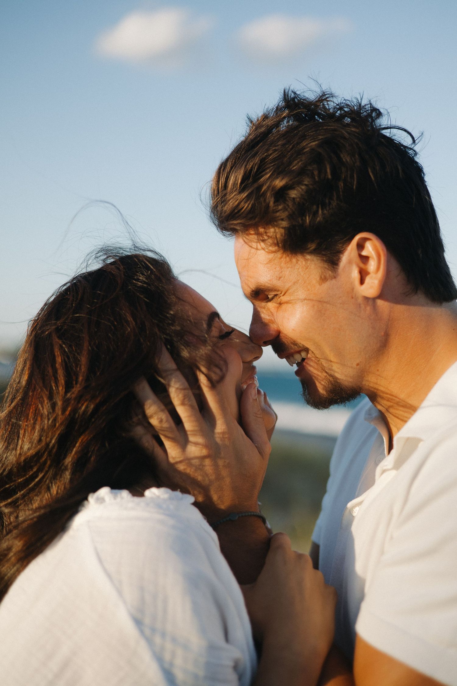 Image of a man holding his girlfriend's face in his hands while they both smile and touch noses