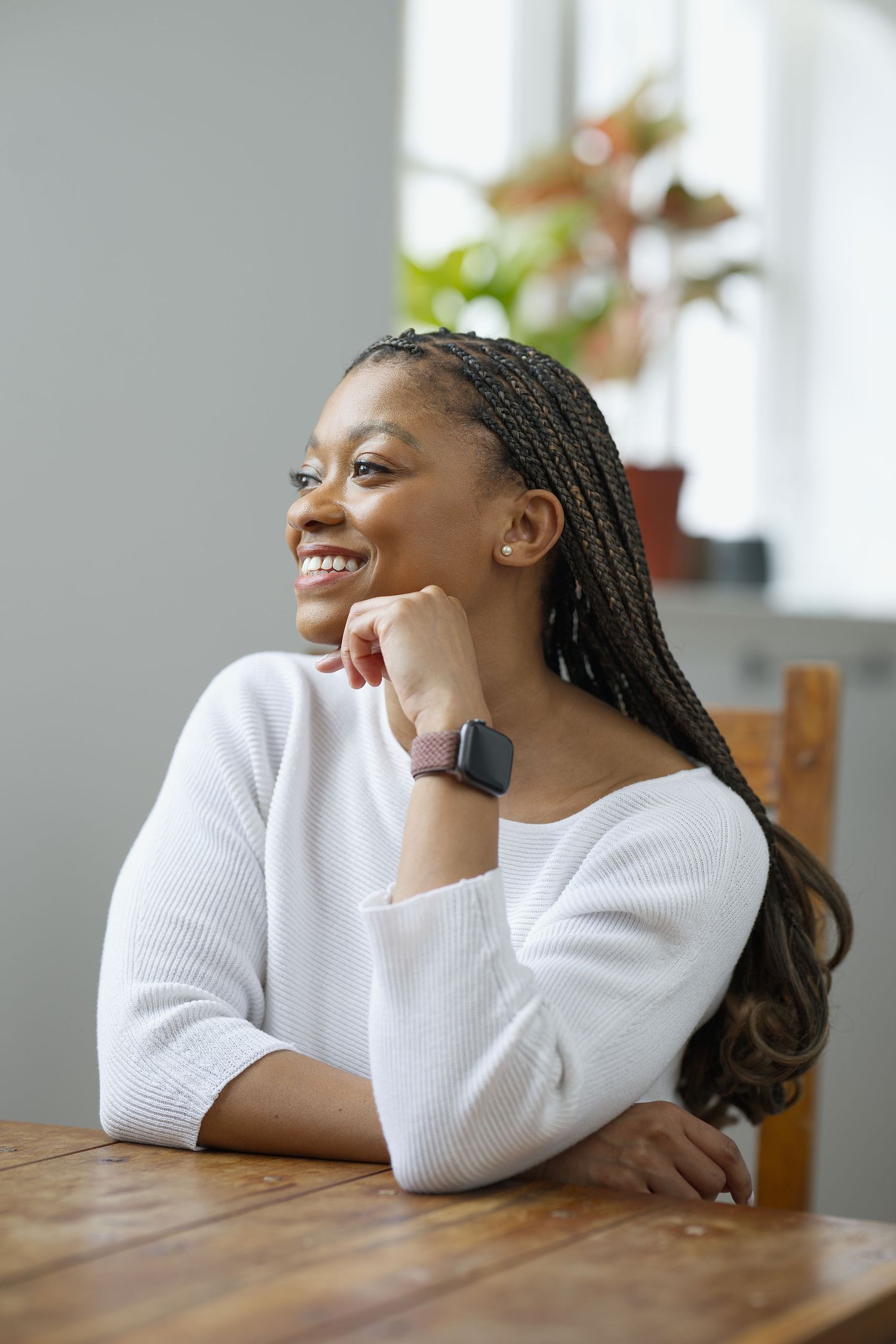 Casual portrait at wooden table wearing white sweater and smartwatch in bright interior.