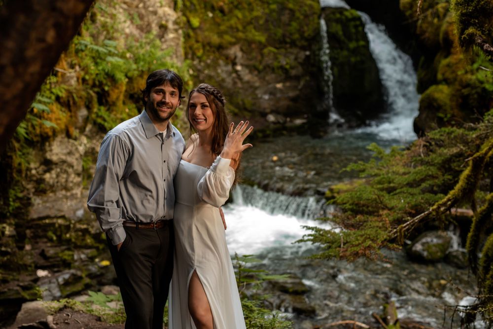 A couple poses by a cascading waterfall in formal attire during an engagement photoshoot.