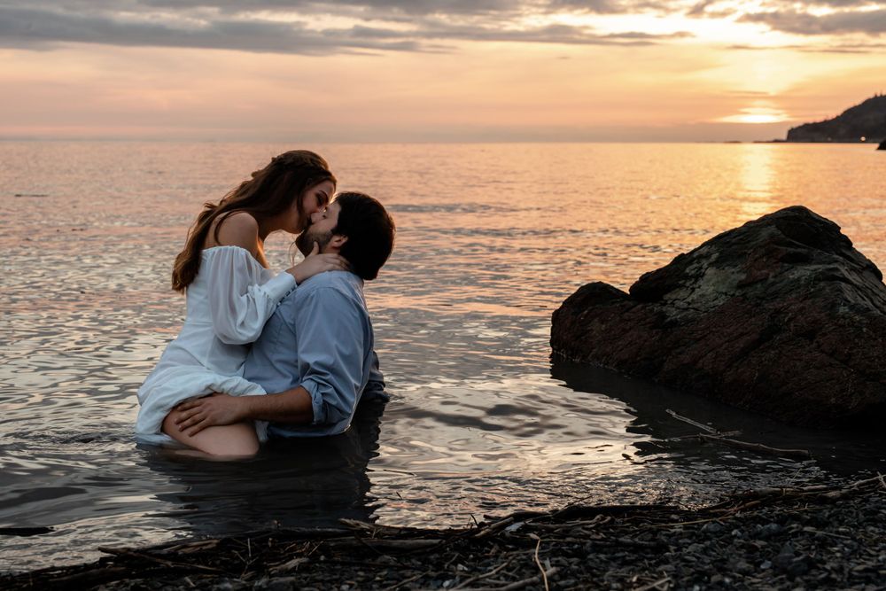 Romantic couple sharing intimate moment on rocky beach at sunset.